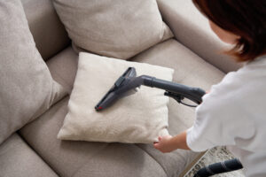 young housewife cleaning sofa with vacuum cleaner living room