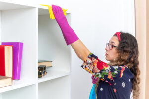 happy woman rubber gloves wiping white shelves with yellow rag using cleaning spray home light living room